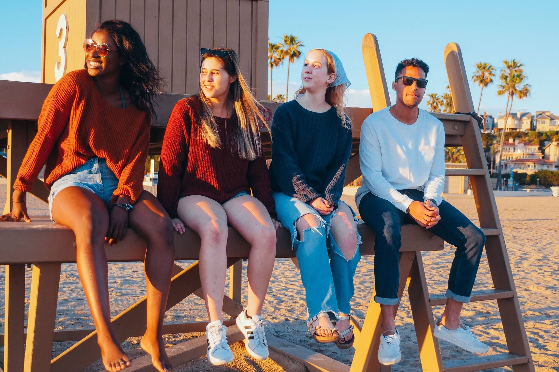 Four young adults sitting together on a lifeguard tower at sunset
